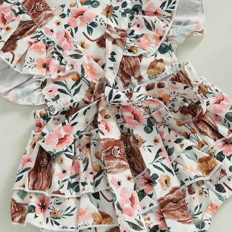 Baby girl in a cow print romper with a matching headband, Western cowgirl baby clothing by Nova Mart.