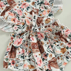Baby girl in a cow print romper with a matching headband, Western cowgirl baby clothing by Nova Mart.