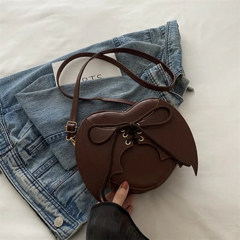 Nova Mart heart-shaped bag with bat wing design, one-shoulder crossbody style featuring a unique strap and bold gothic details.
