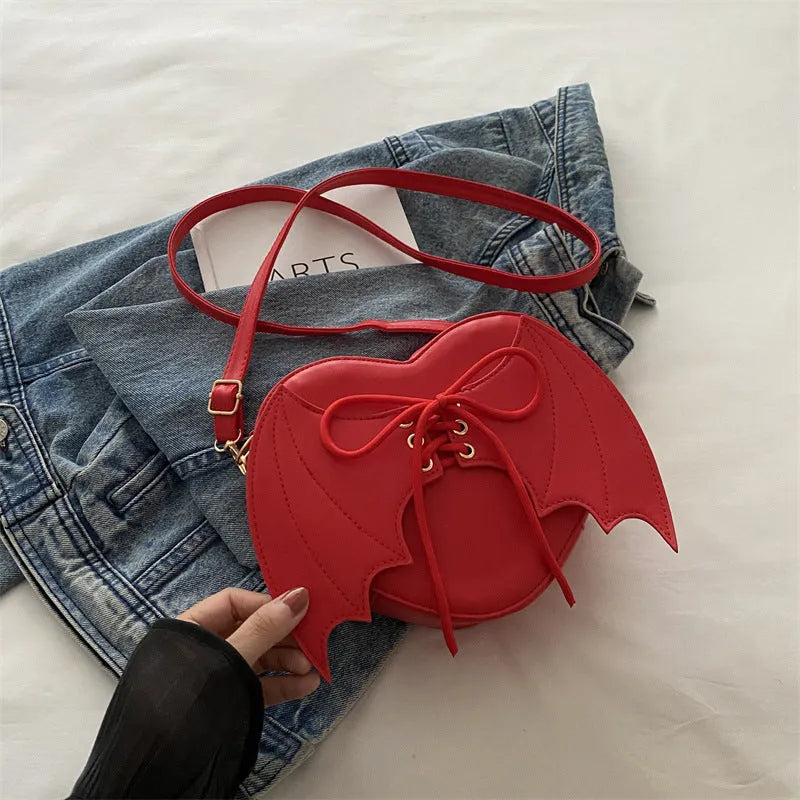 Heart-shaped bag with bat wing design, one-shoulder crossbody strap, black color, stylish accessory from Nova Mart.